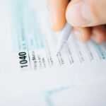 Close-up of a hand using a pen to fill out a tax form 1040, focusing on details.